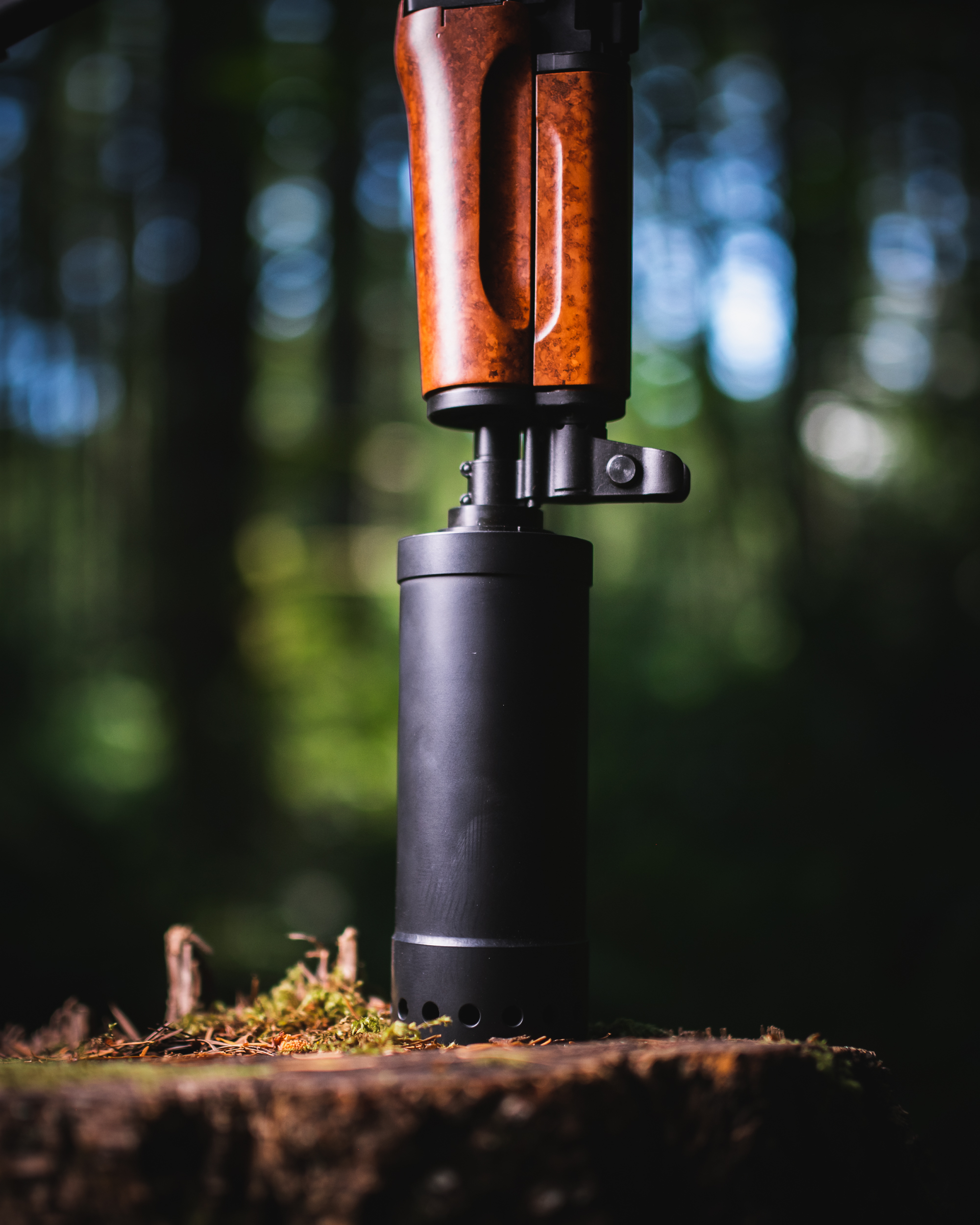 Suppressed rifle standing on a mossy stump in the forest