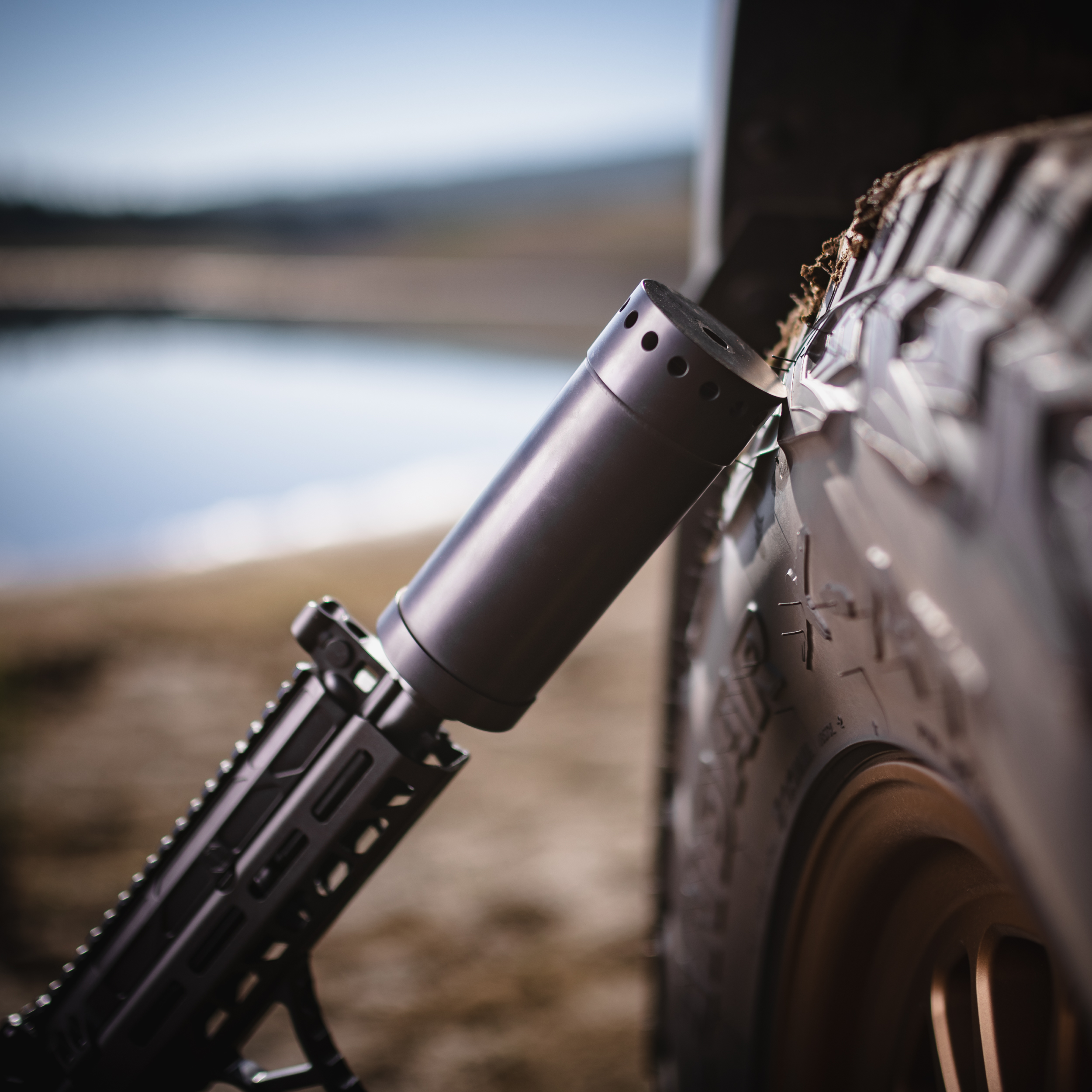 Resilient suppressor mounted on a rifle, leaned against an off-road tire